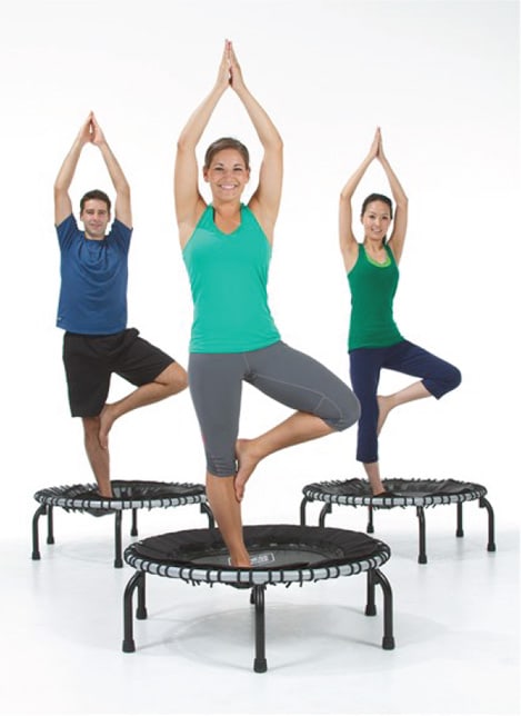 3 people, each standing in yoga pose, with hands over head and one leg making triangle with other leg, on their own JumpSport fitness trampoline