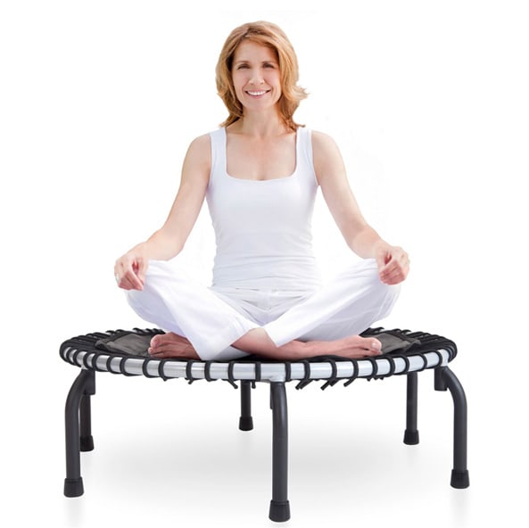 Middle aged women smiling and sitting in the lotus position on a JumpSport fitness trampoline